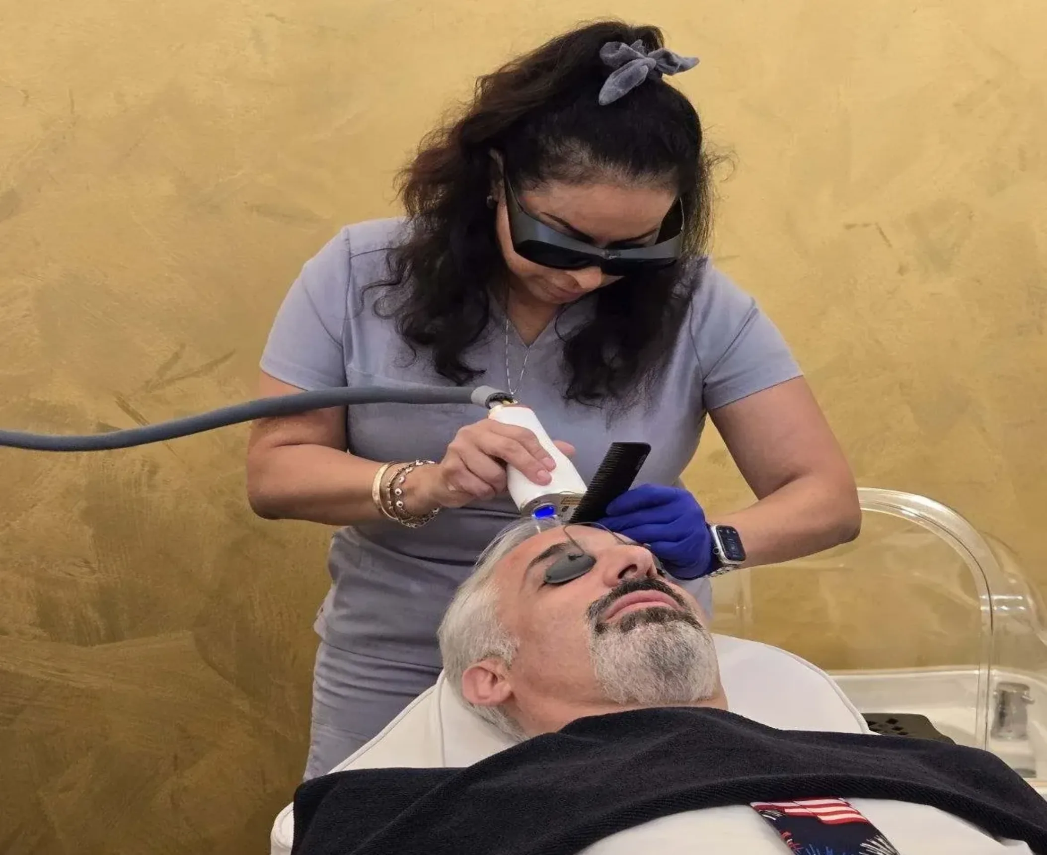 A healthcare professional performs a treatment on a patient lying down, with modern equipment in a serene, gold-toned environment